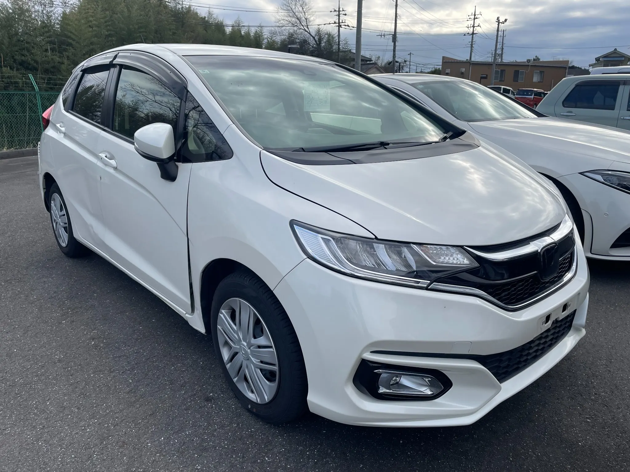 White Honda Fit hatchback front side view parked in a used car lot